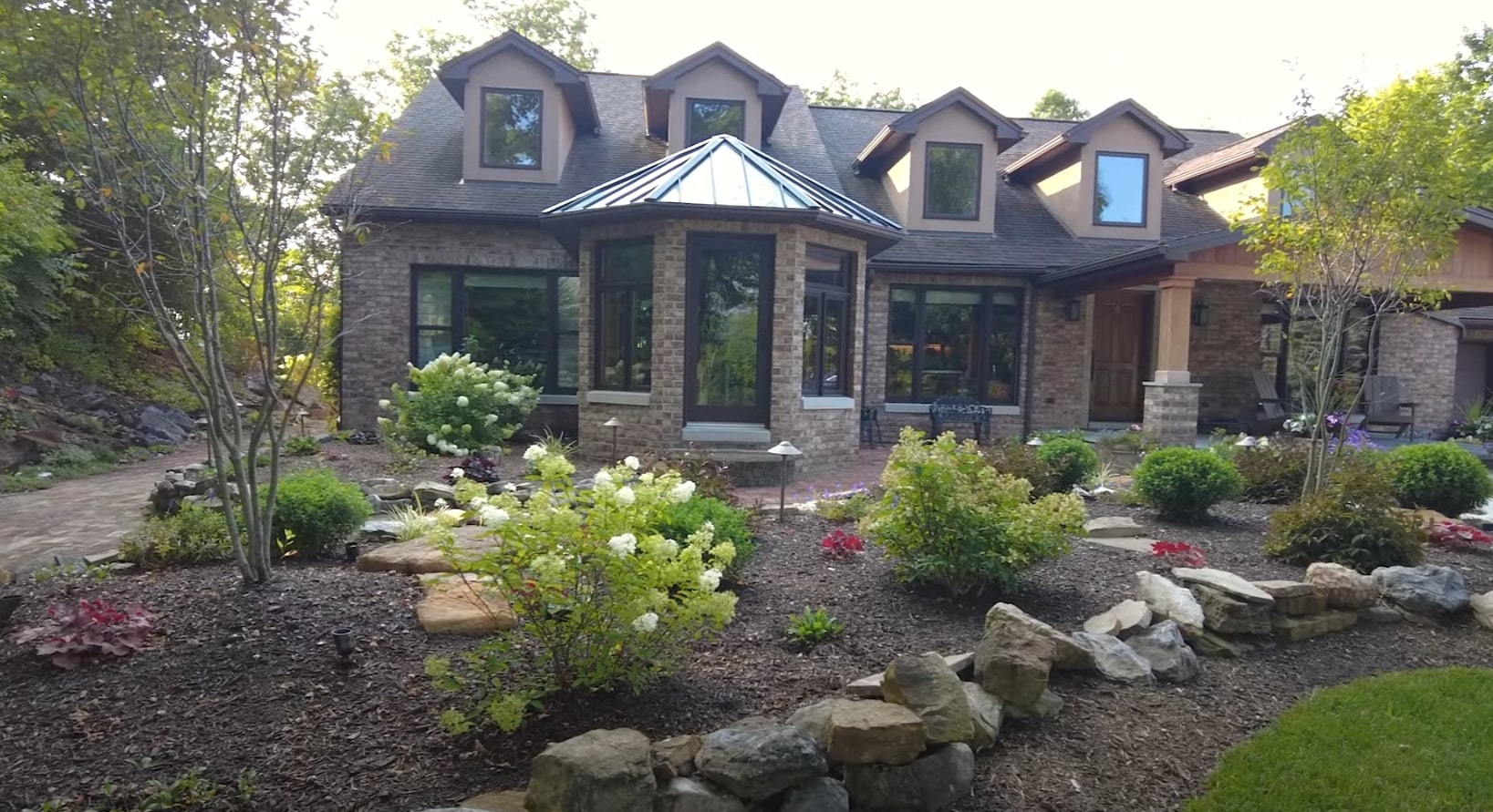 Complete Front Yard Transformation with Stone and Plant Design Elegant residential front yard landscaping with natural stone features, colorful flowering plants, manicured lawn, and professionally designed garden beds