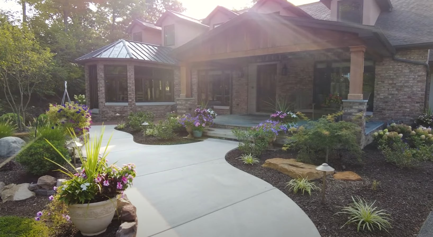 Front Yard Landscape Design with Hardscaping Elements Modern home front entrance with professional landscaping featuring curved concrete walkway, planted garden beds, decorative containers, and stone accents