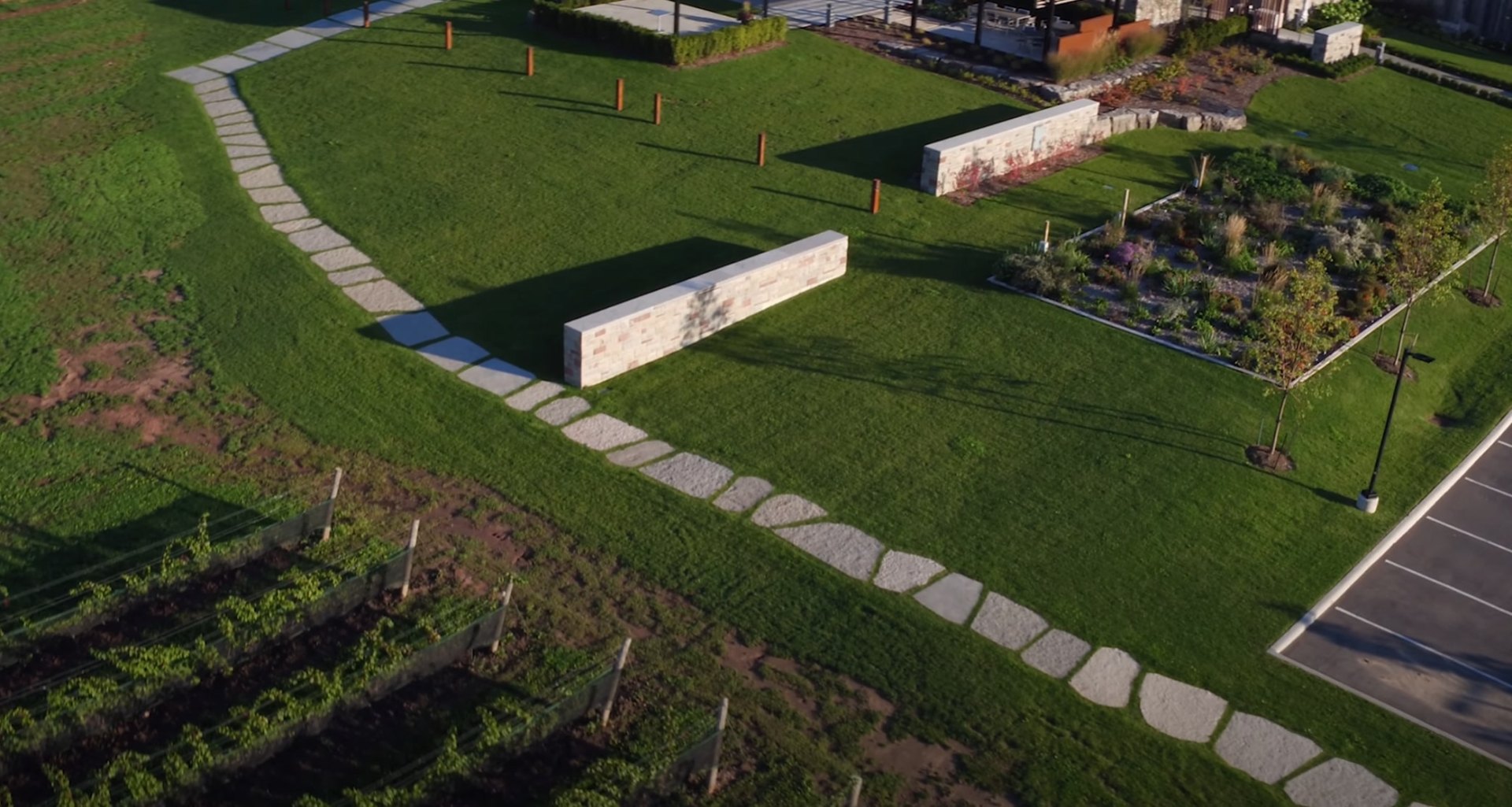 Comprehensive Landscape Design with Pathways and Retaining Walls Aerial landscape view showing stone pathway through green lawn, retaining walls, and organized garden areas demonstrating professional landscape planning
